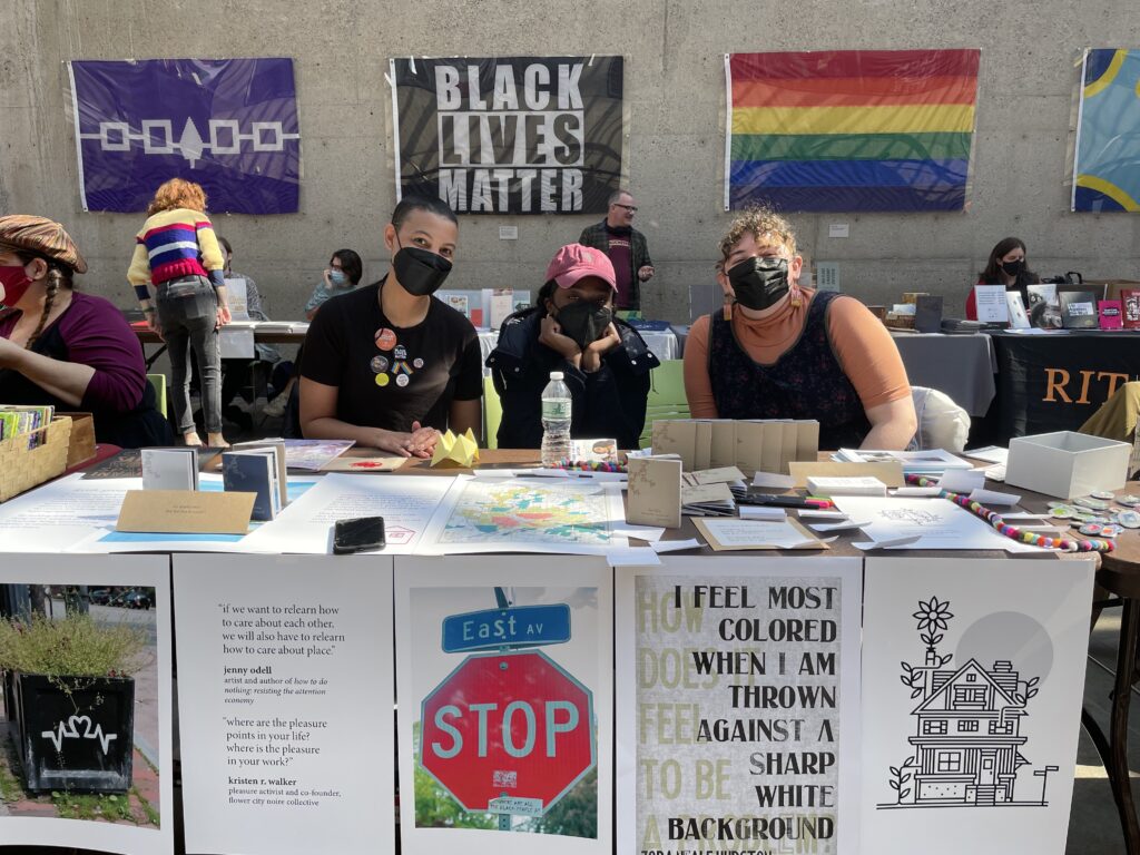 three young people sit behind a table underneath indigenous, blm, and pride posters